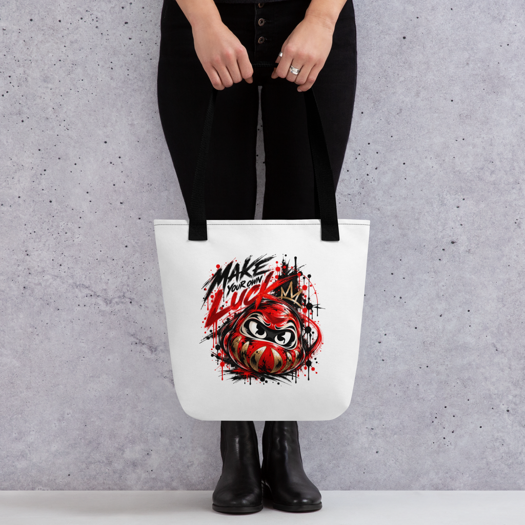 White tote bag featuring a colorful Daruma graphic with the text "MAKE YOUR OWN LUCK." Double black cotton handles.
