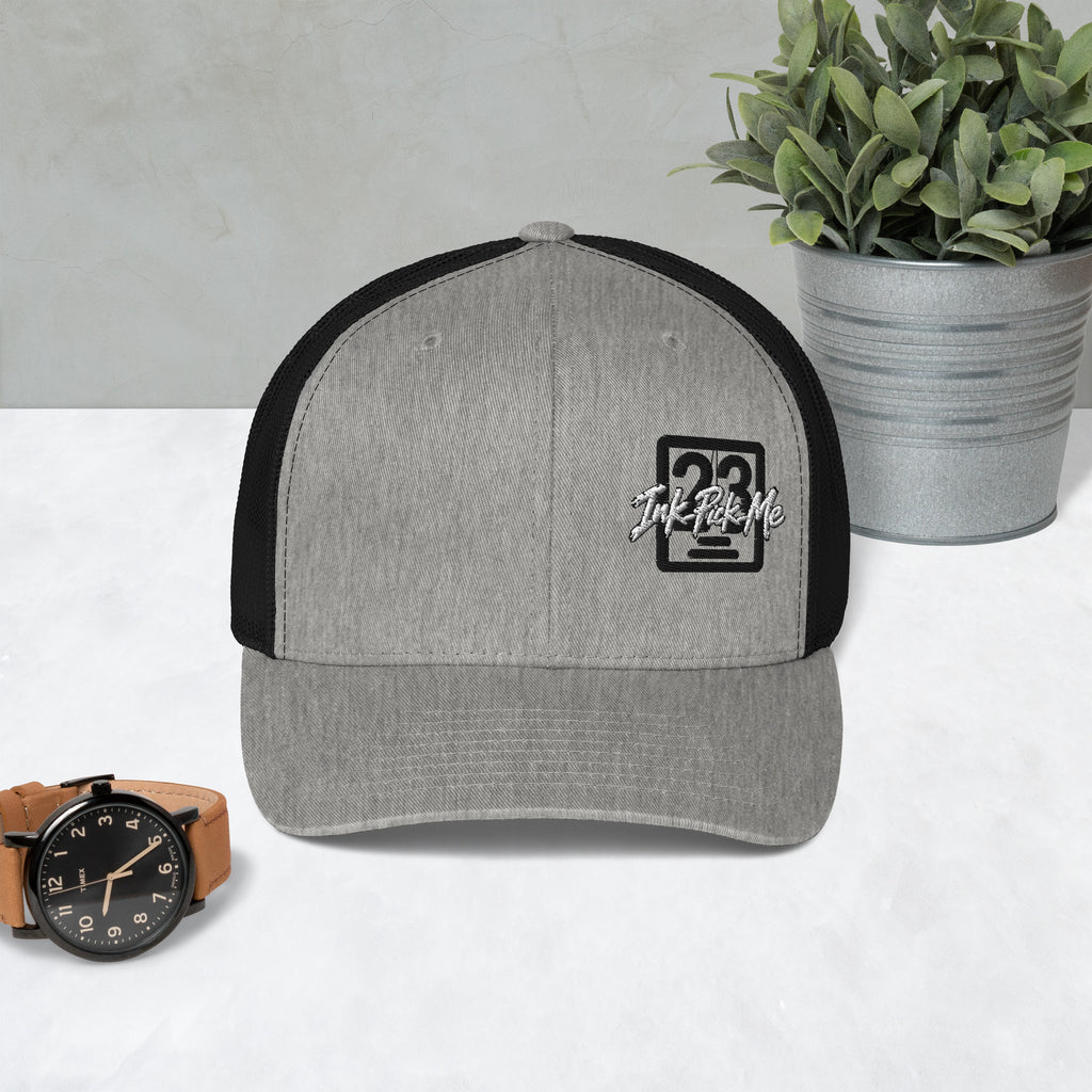 Casquette trucker Signature gris chiné et noir Ink Pick Me posée sur une table – vue de face