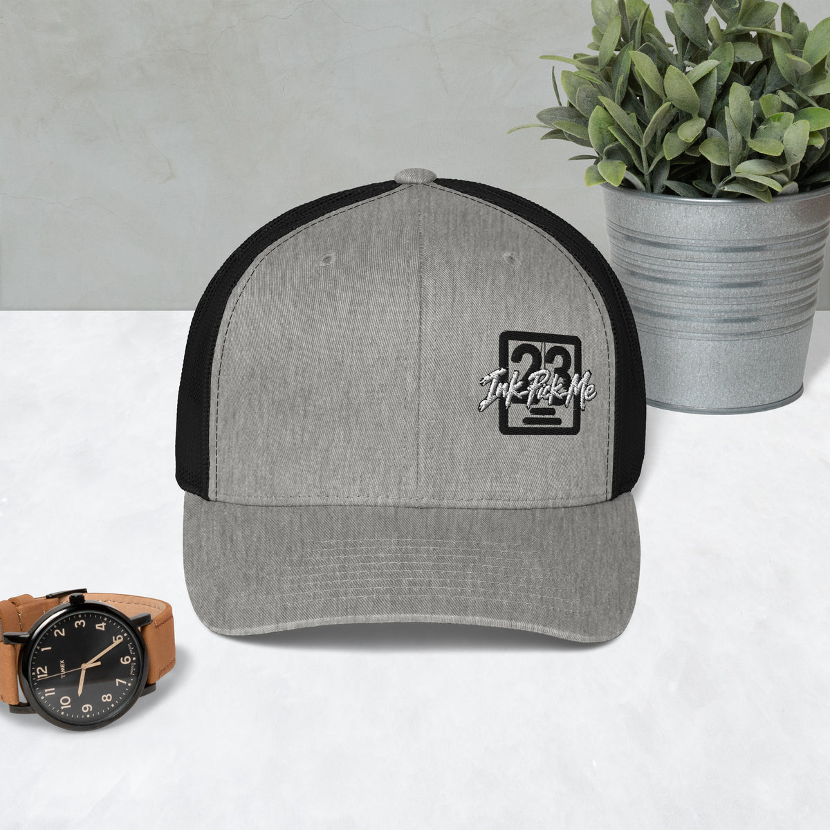 Casquette trucker Signature gris chiné et noir Ink Pick Me posée sur une table – vue de face
